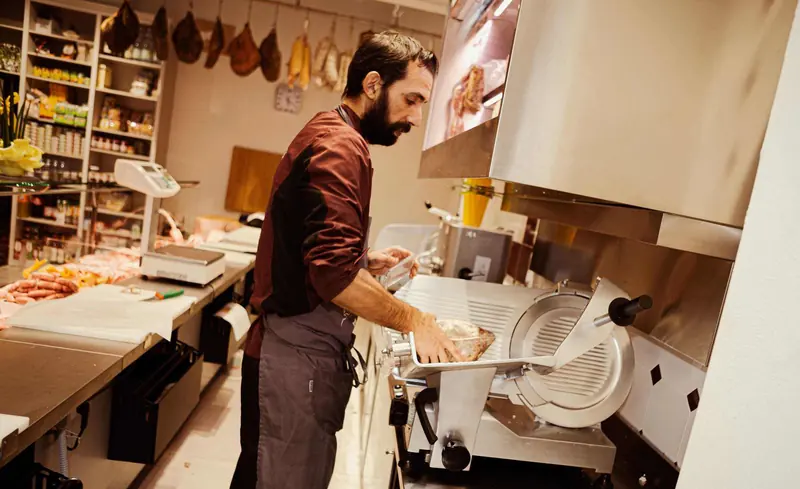 Affettatrice e prosciutti appesi nel negozio